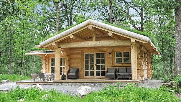 Una cabaña de madera con porche, mobiliario exterior y cimientos de piedra.
