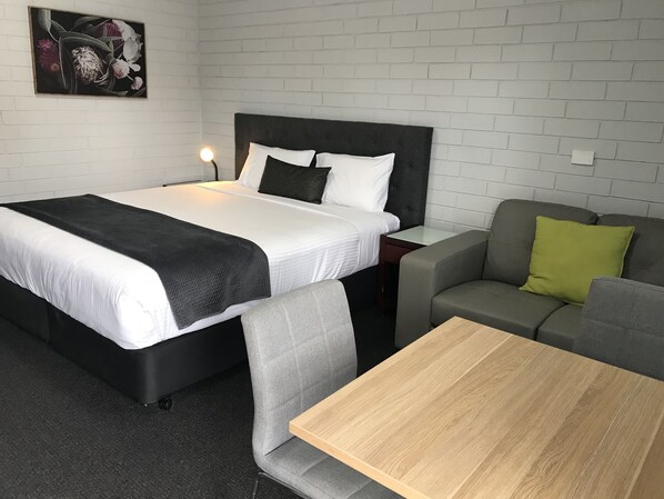 Una habitación de hotel con una cama, una mesita de noche, un sofá gris, una mesa de madera y un cuadro colgado en la pared.