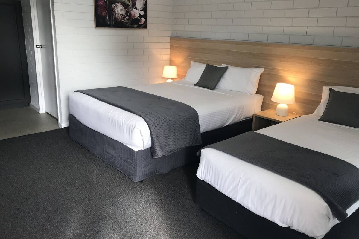 Hotellihuone, jossa on kaksi sänkyä, valkoiset seinät, puinen sängynpääty ja taulu sänkyjen yläpuolella.