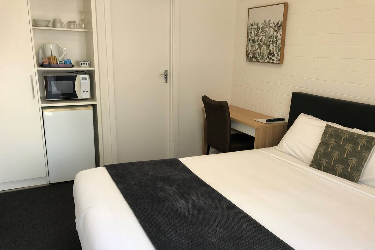 Hotellihuone, jossa on sänky, työpöytä, tuoli, mikroaaltouuni ja jääkaappi.
