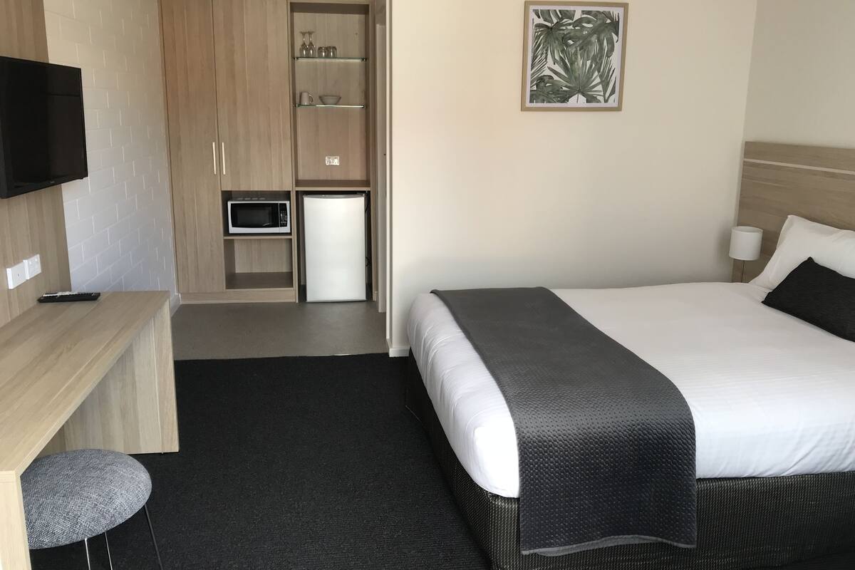 Hotellihuone, jossa on sänky, työpöytä tuolilla, mikroaaltouuni ja televisio.