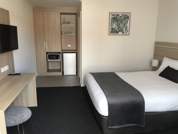 A hotel room with a bed, a desk with a chair, a microwave, and a TV.
