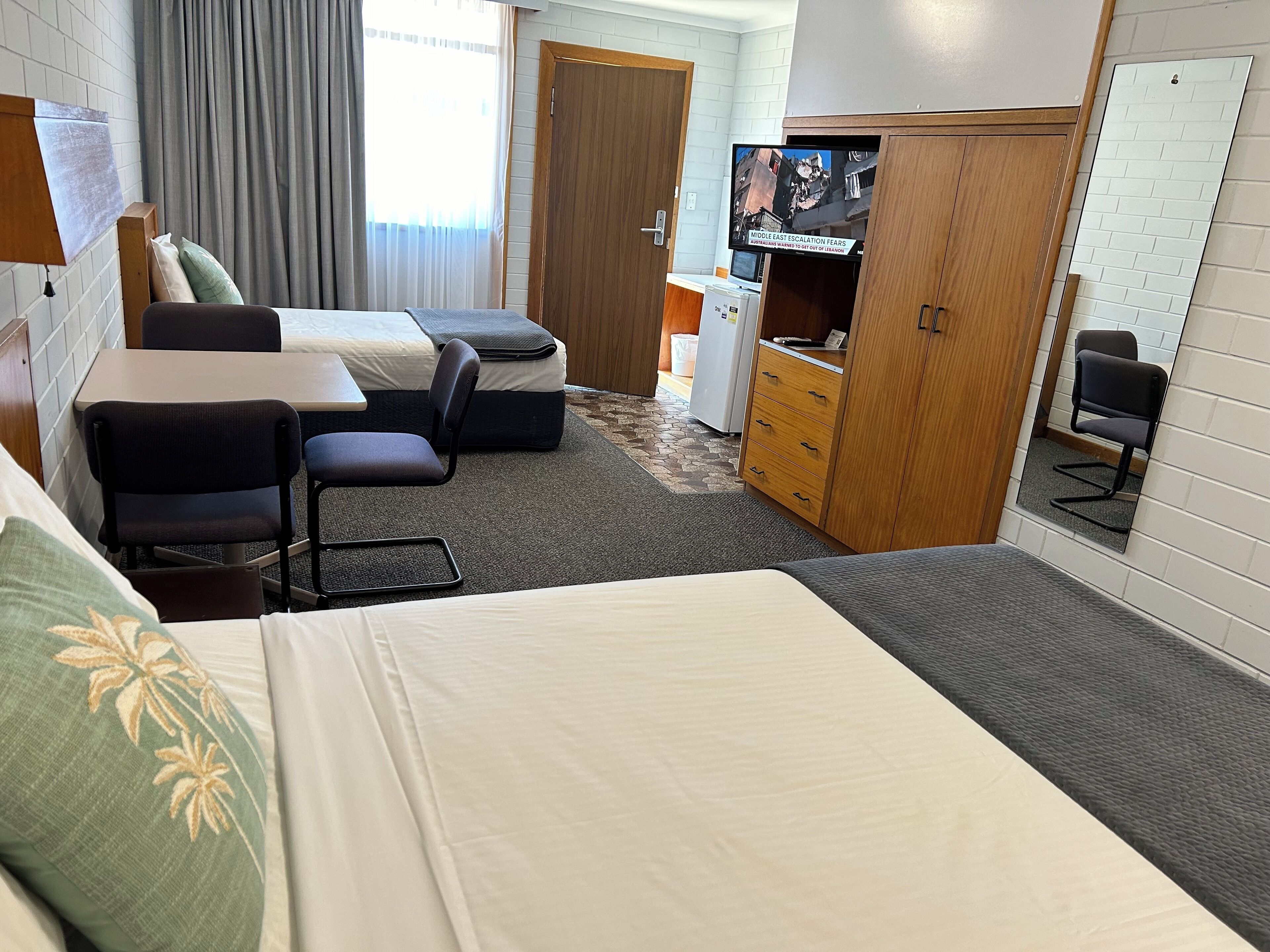 A hotel room with a bed, a desk, a chair, a TV, and a wardrobe.