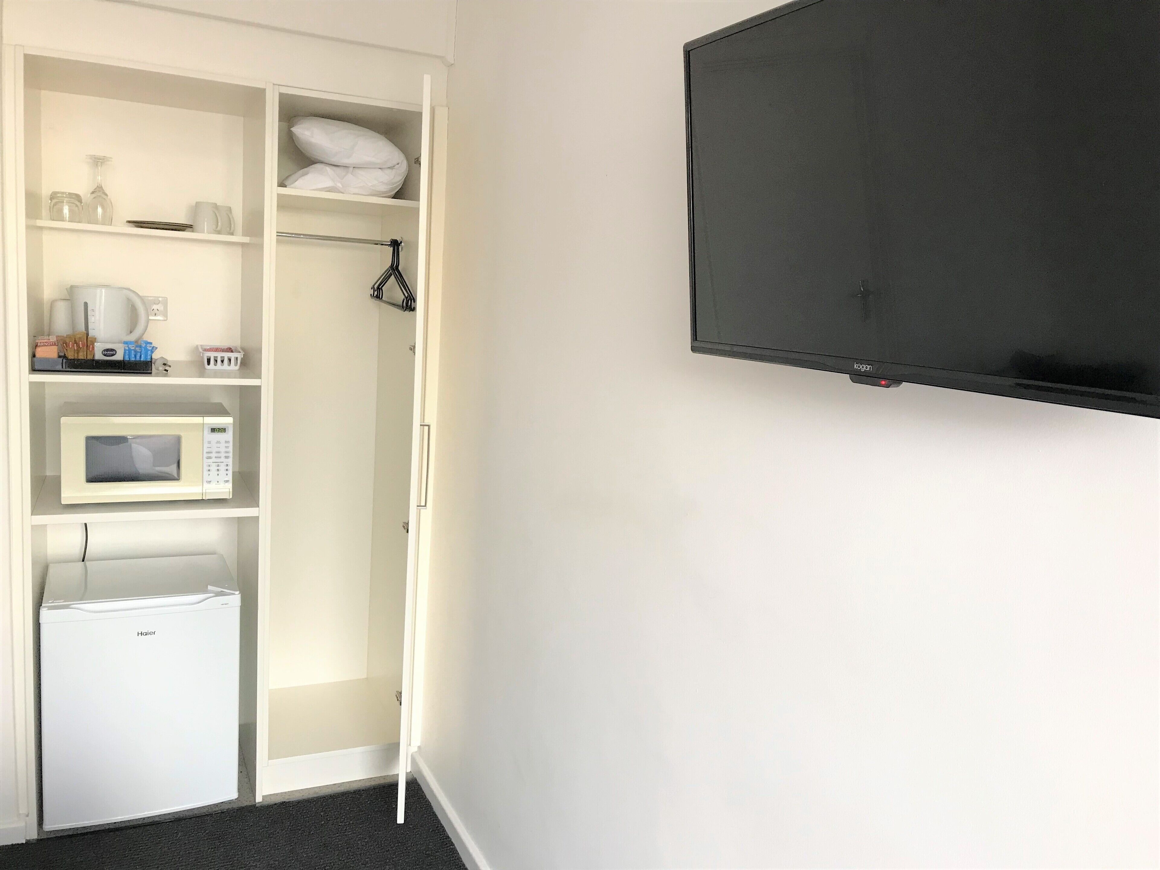 A compact kitchenette with a microwave, a small refrigerator, and a shelf with kitchen essentials.