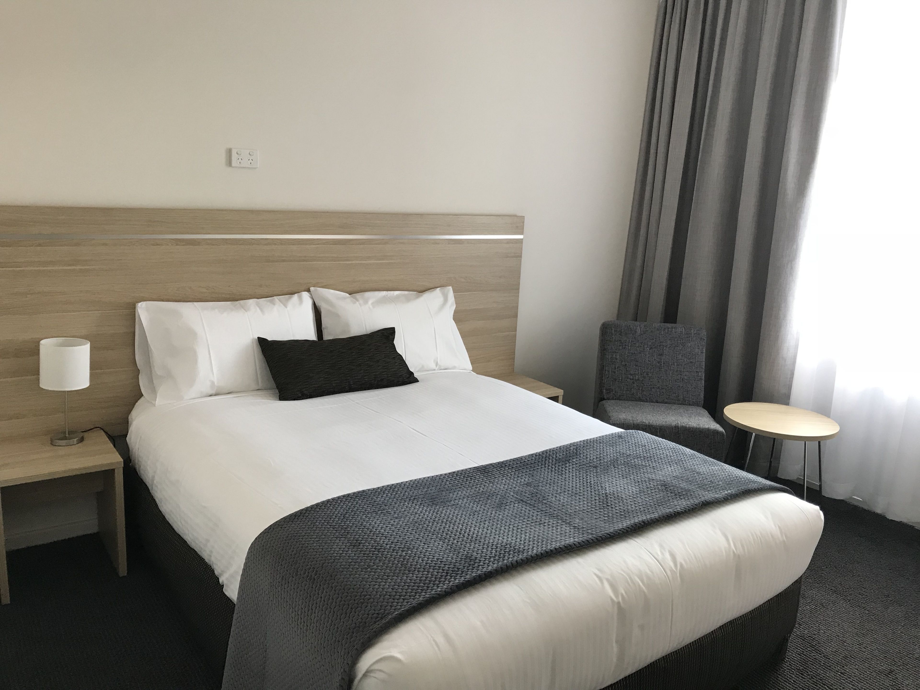 A hotel room with a bed, a nightstand, a chair, and a small table.