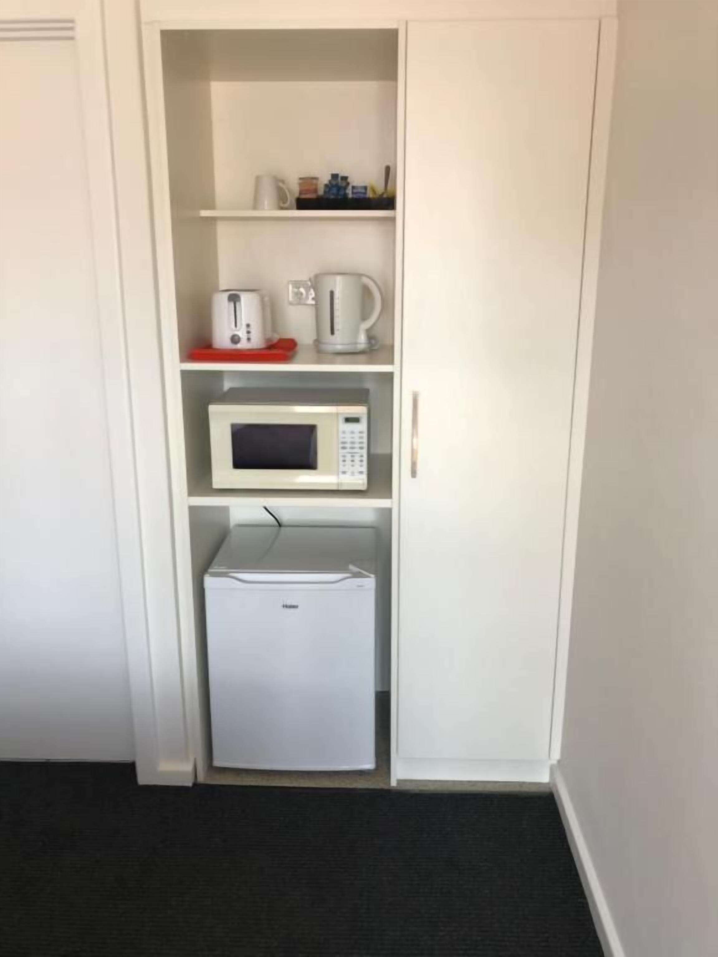 Eine kompakte Küchenzeile mit Mikrowelle, Toaster und Kaffeemaschine auf den Regalen, sowie einem kleinen Kühlschrank darunter.