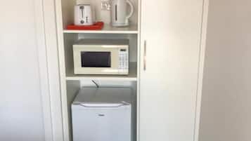 Uma cozinha compacta com micro-ondas, torradeira e cafeteira nas prateleiras, e uma pequena geladeira embaixo.