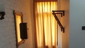 Un pasillo estrecho con pared de ladrillo blanco, un banco de madera, una mesa con una botella y una puerta al final.