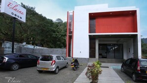 Un hotel moderno llamado "Elaine", con fachada blanca y roja, autos estacionados y cielo despejado.