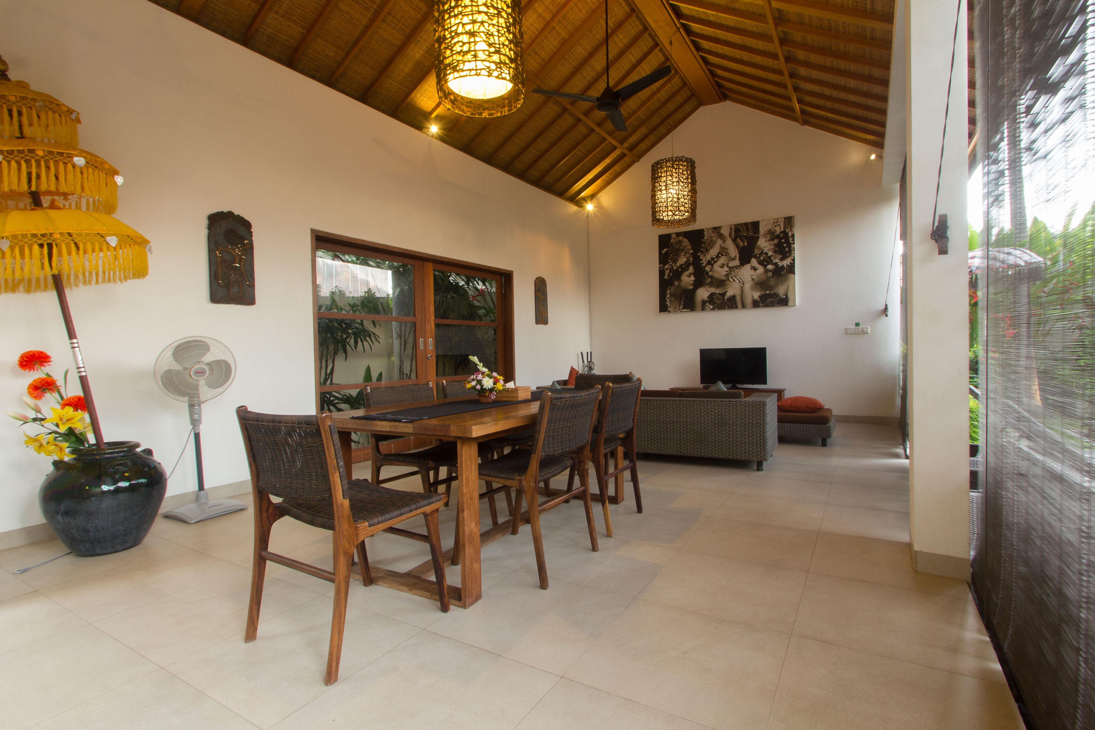 A dining area with a wooden table and chairs, a fan, and a decorative vase with flowers.