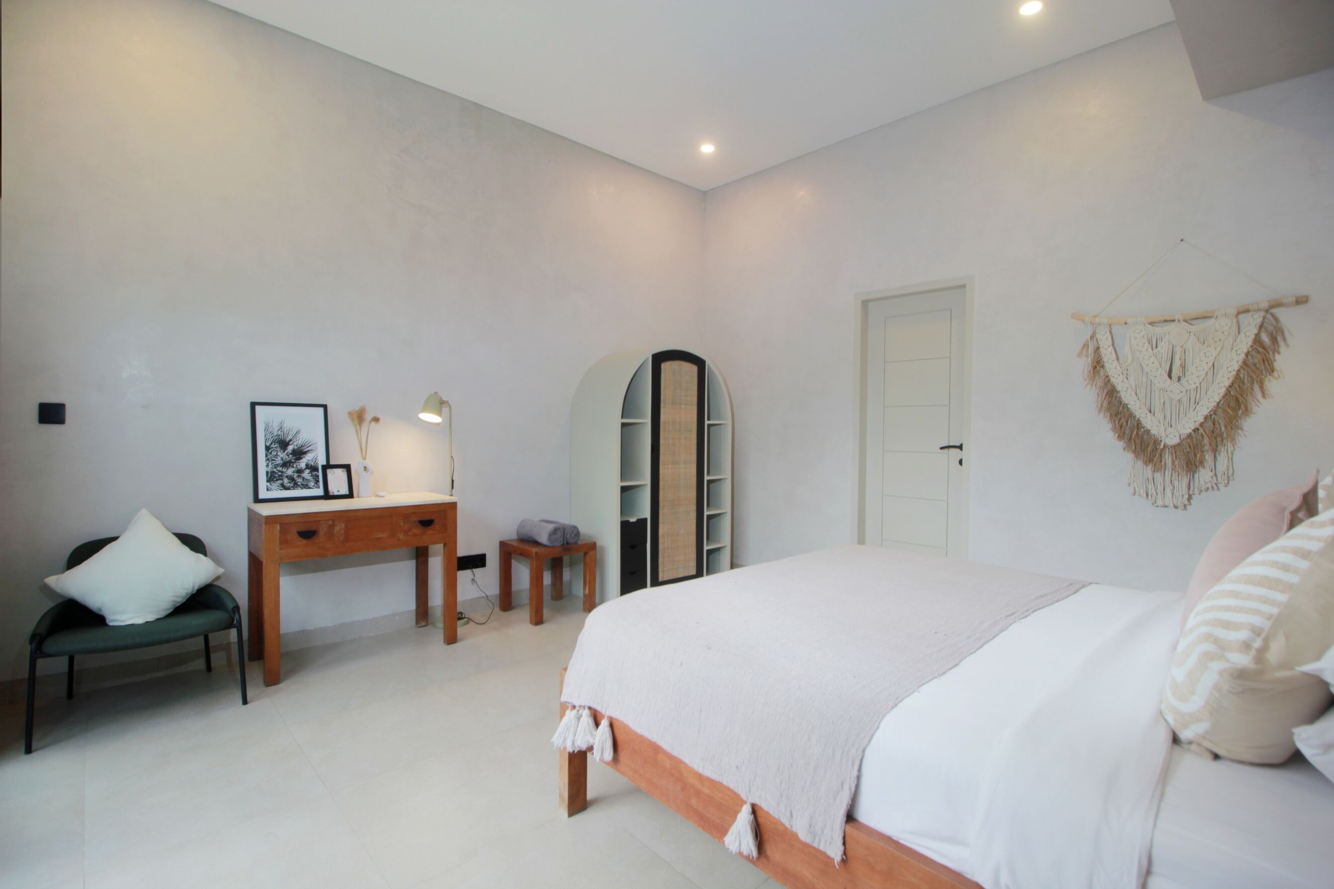 Un dormitorio con cama, escritorio, silla, armario y un adorno de macramé en la pared.