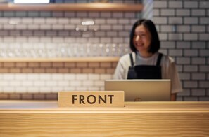 A wooden counter with a sign reading "FRONT" and a person sitting behind it with a laptop. - 9 C Hotel Asahikawa (Asahikawa)