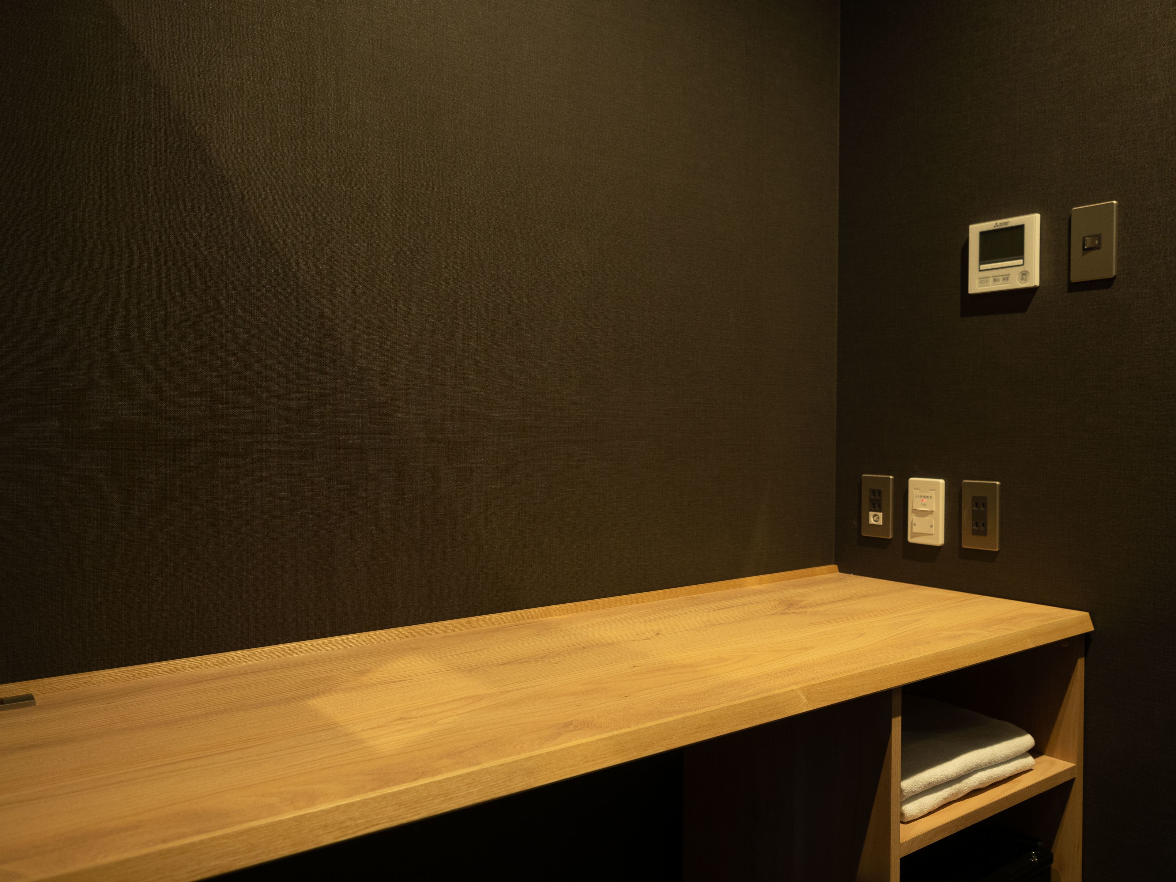 Un banco de madera con un estante debajo, una pared oscura y tres enchufes.