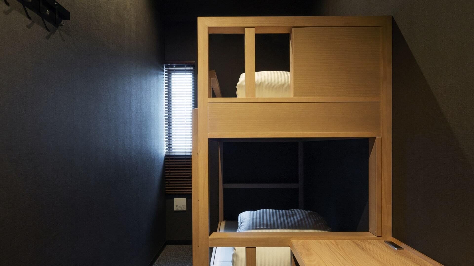 Una cama litera con escritorio y ventana con persianas.