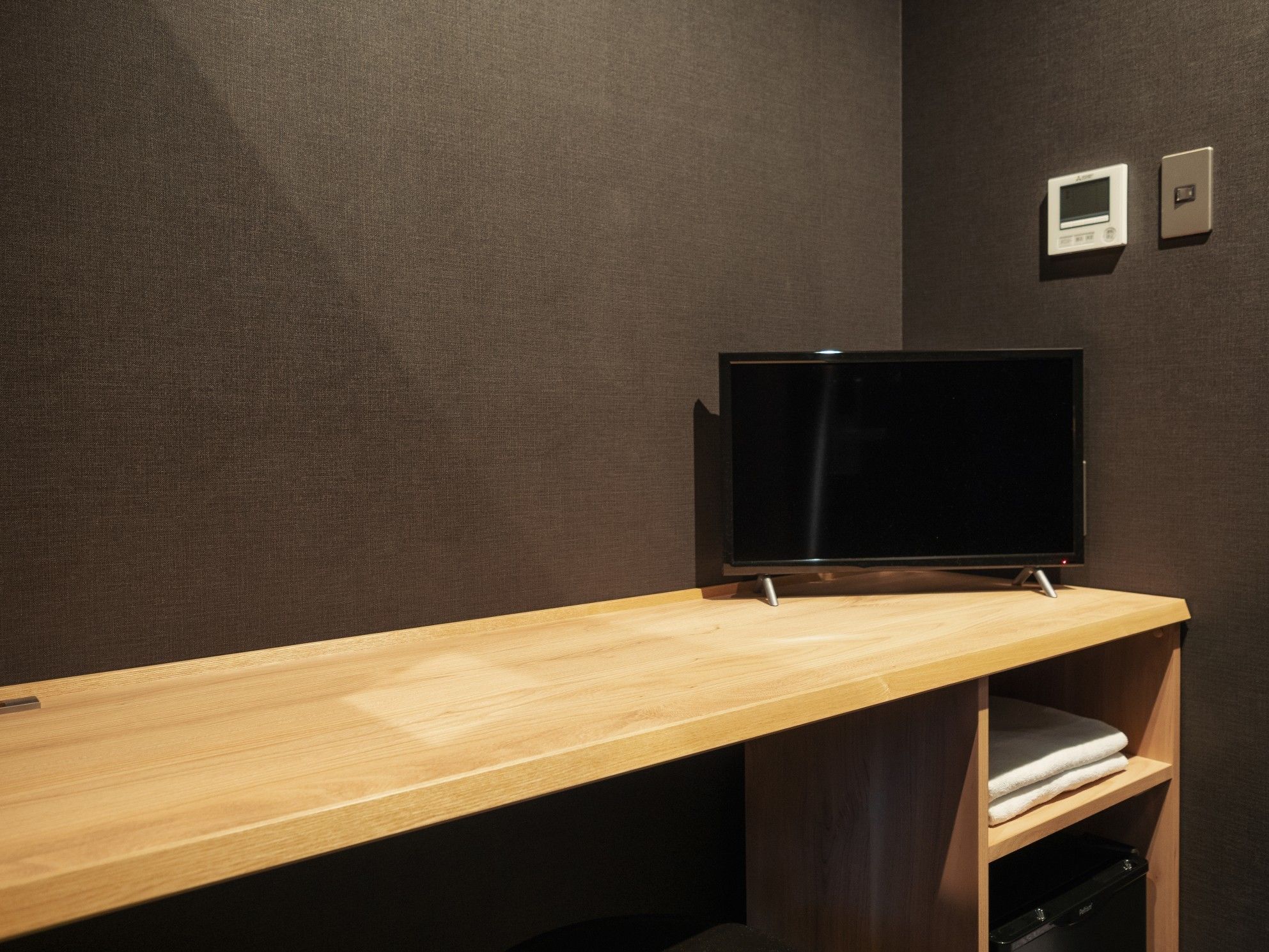 A modern room with a wooden desk, a flat-screen TV, and a built-in shelf with a folded towel.