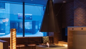 A modern lounge area with a fireplace, leather seating, and a large window overlooking a snowy street. - 9 C Hotel Asahikawa (Asahikawa)