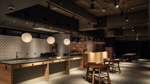 A modern kitchen with a brick backsplash, wooden bar counter, and pendant lighting. - 9 C Hotel Asahikawa (Asahikawa)