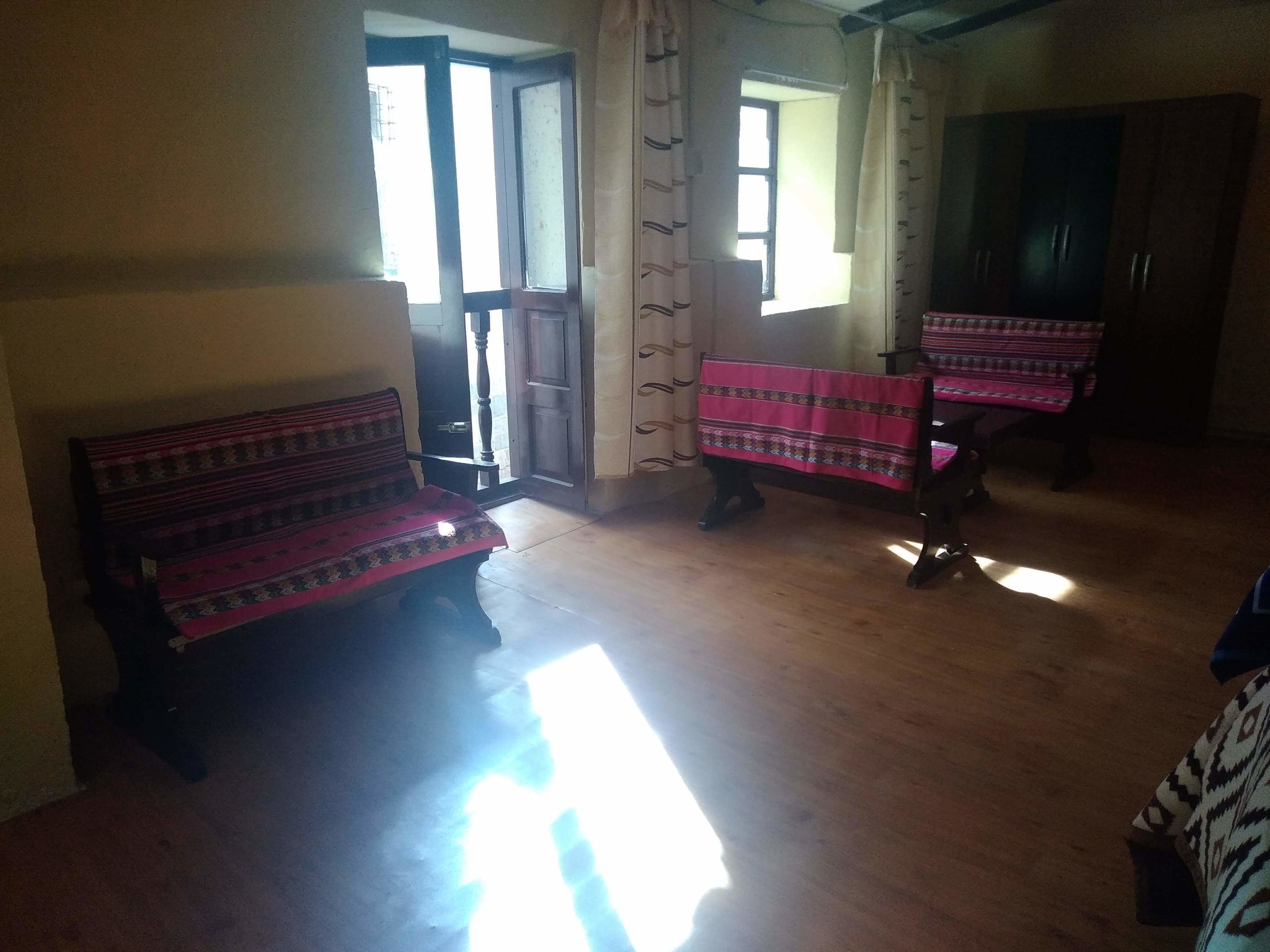 Ein Zimmer mit zwei hölzernen Bänken, die mit gemusterten Stoffen bezogen sind, einem Holzboden und einer Tür, die nach draußen führt.