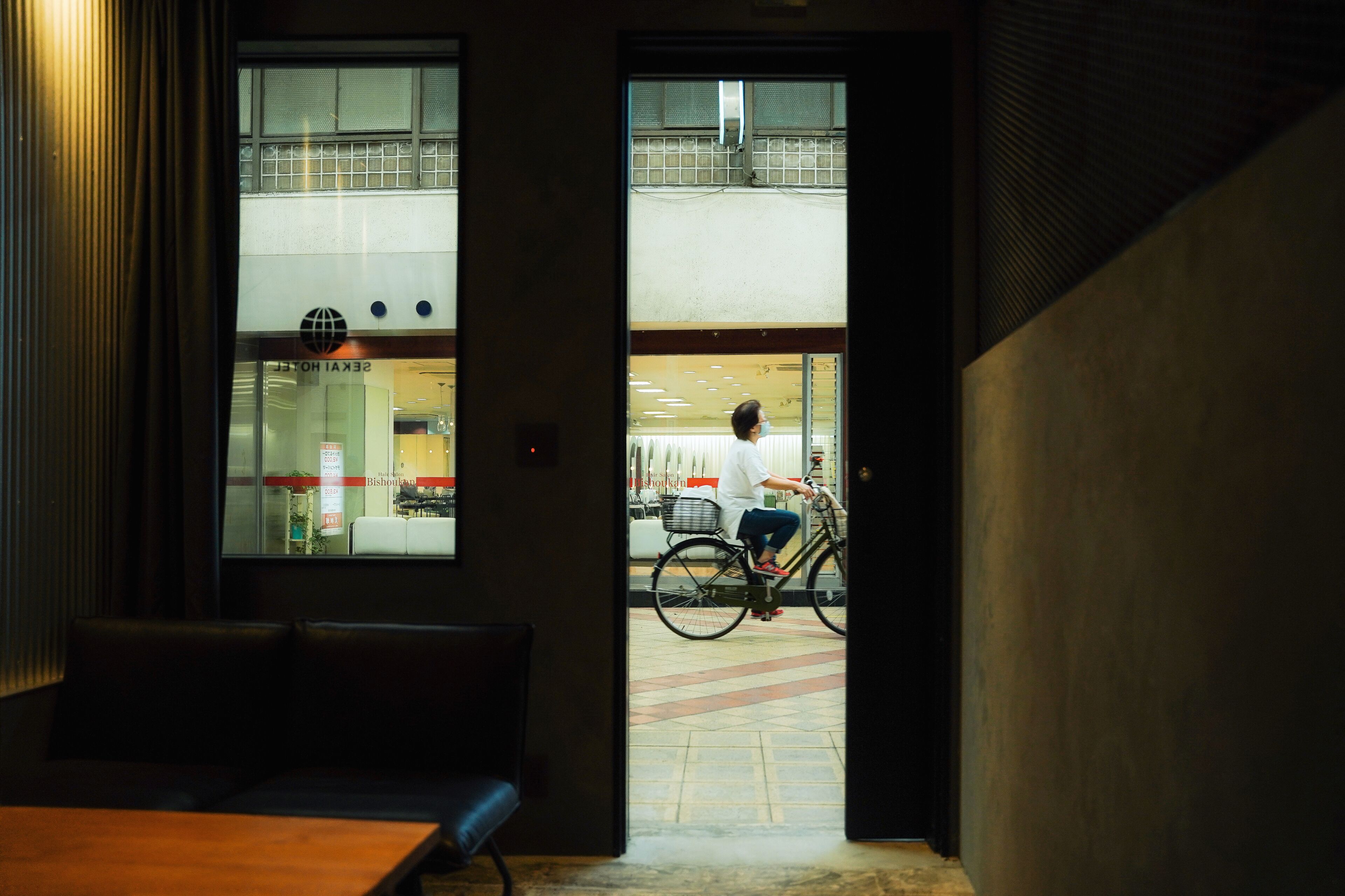 A view from inside a building looking out to a street where a person is riding a bicycle.