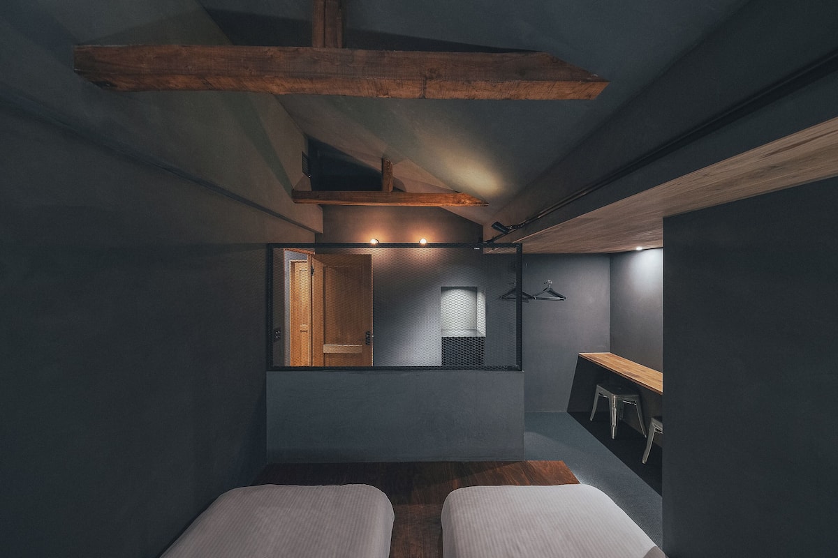 A compact bedroom with a bed, a wooden bench, and a mirror reflecting a bathroom.