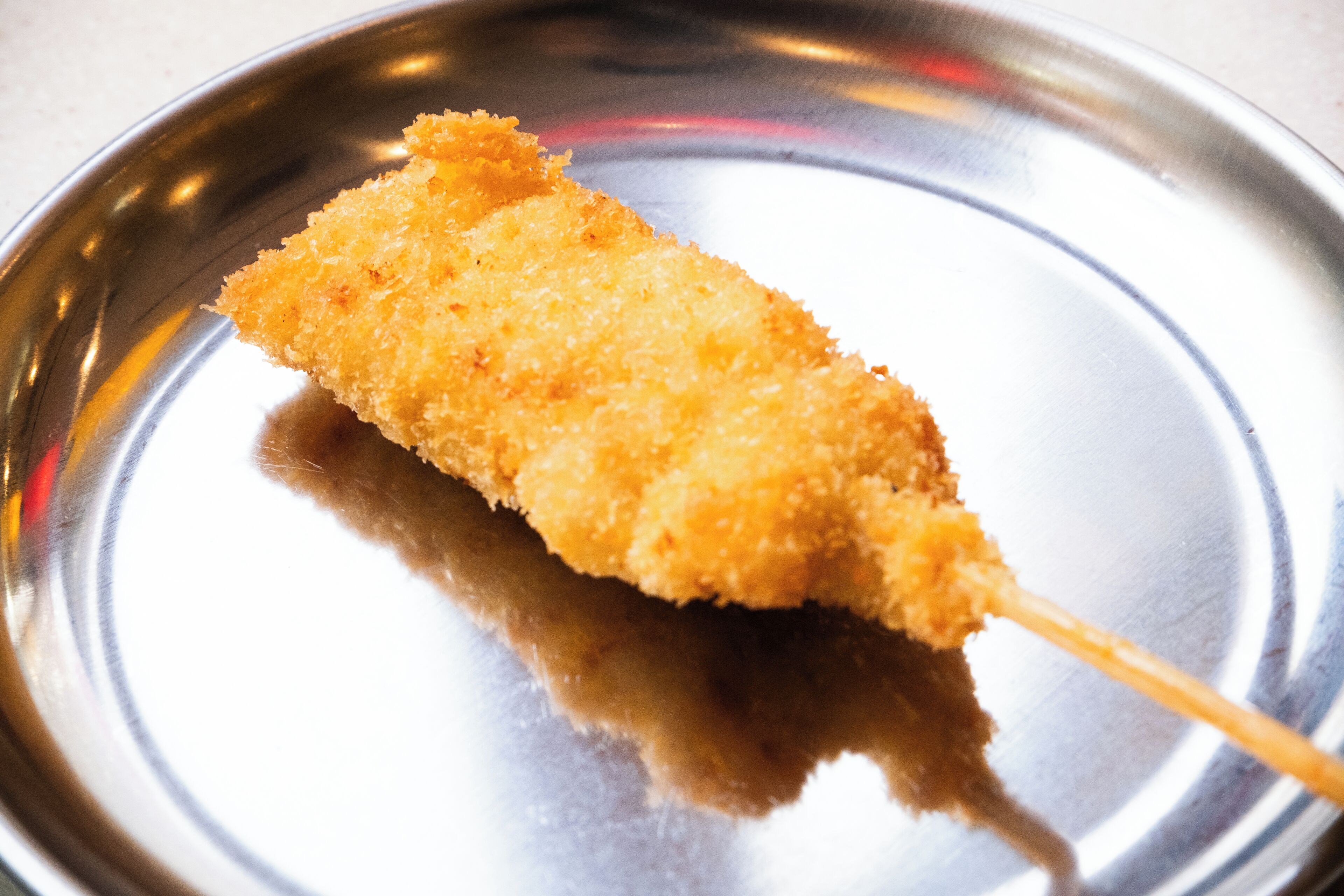 Un perro caliente con palito sobre un plato de metal.