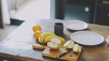 A wooden table with a cutting board, a knife, sliced apples, bananas, and oranges.