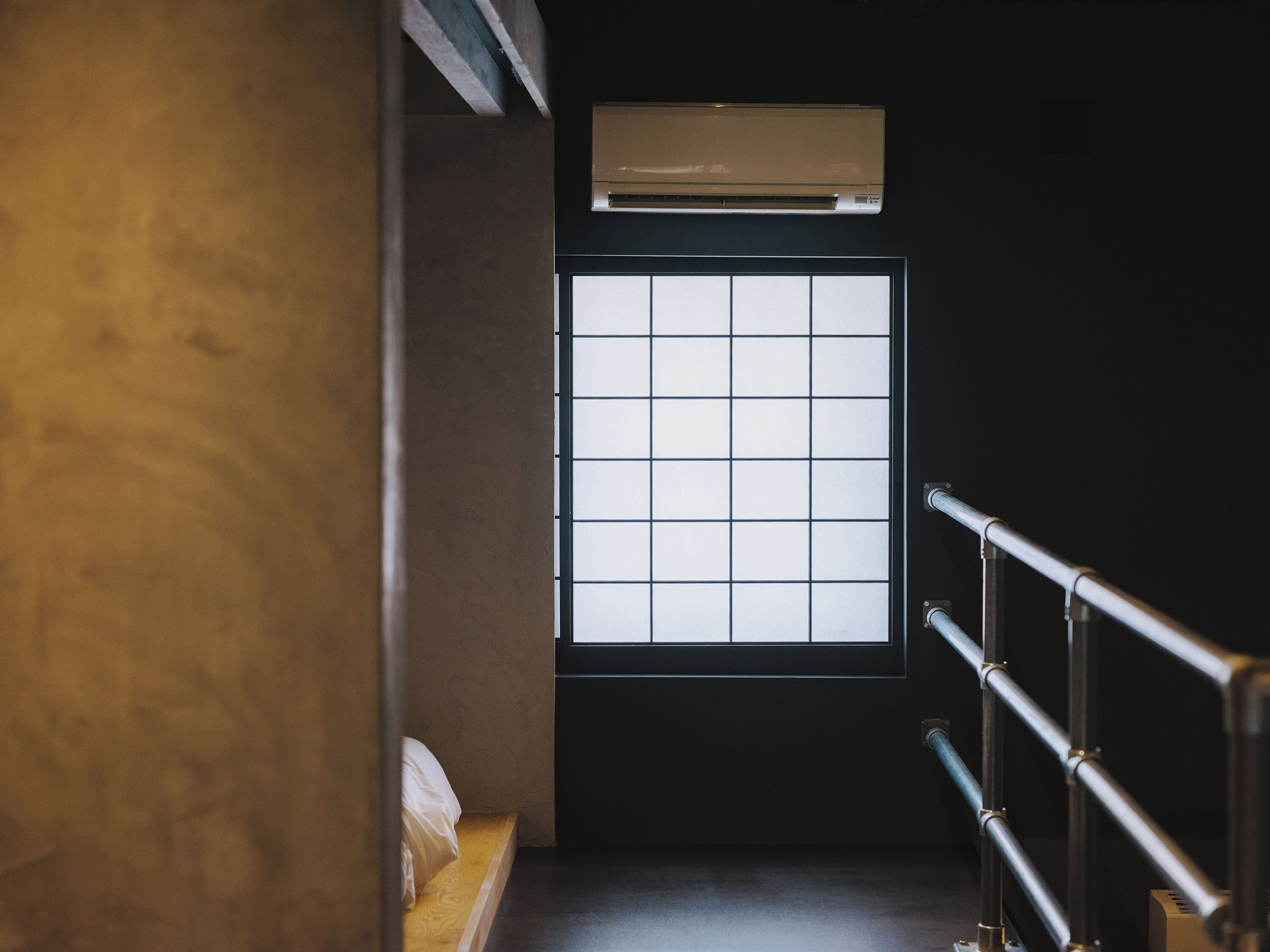 A room with a bed, a window with a grid pattern, and an air conditioning unit above the window.