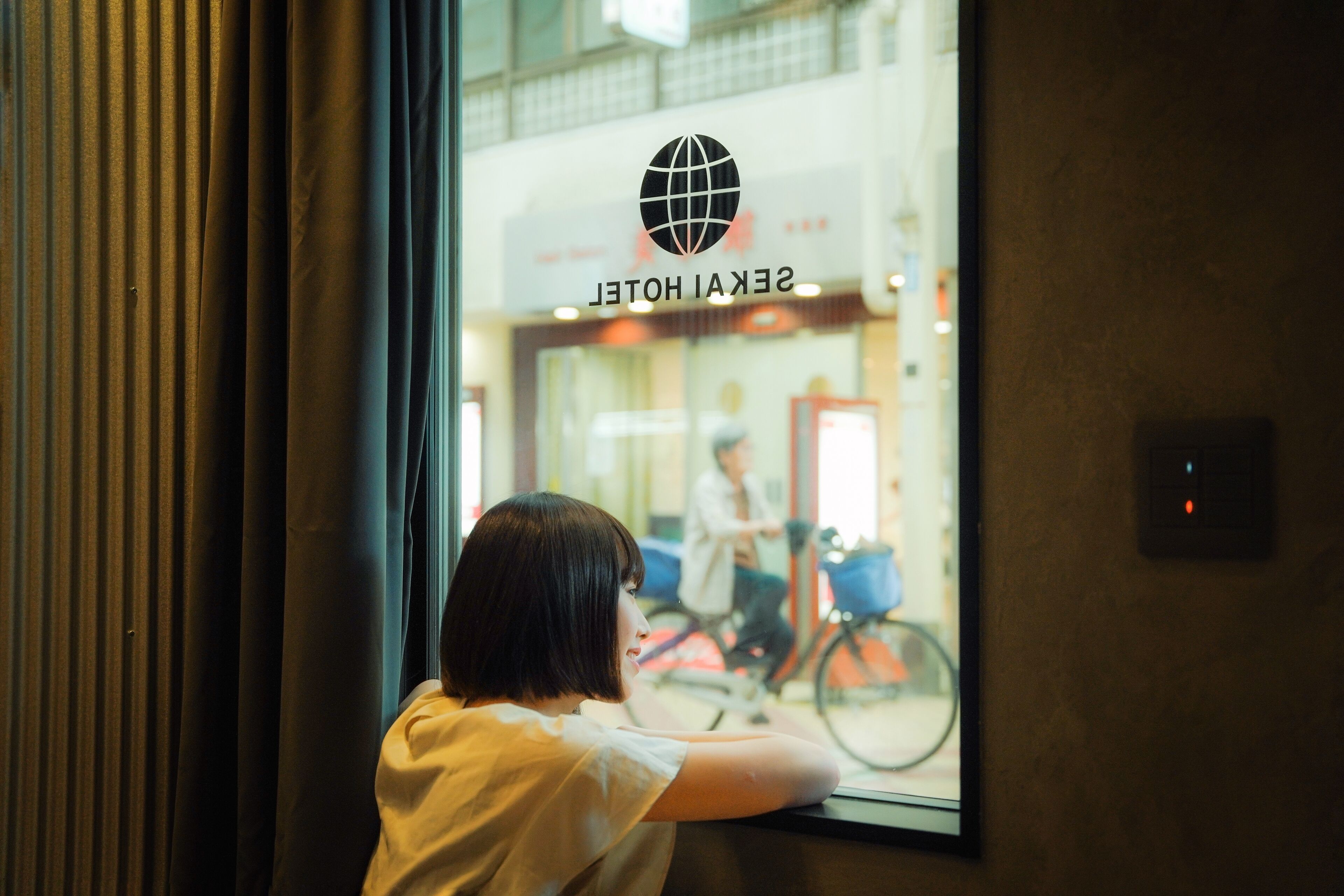 En person som lutar sig mot ett fönster med utsikt över en hotellobby och en cykel som står utanför.