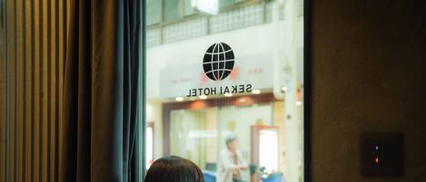 A person leaning on a window with a view of a hotel interior and a bicycle outside.