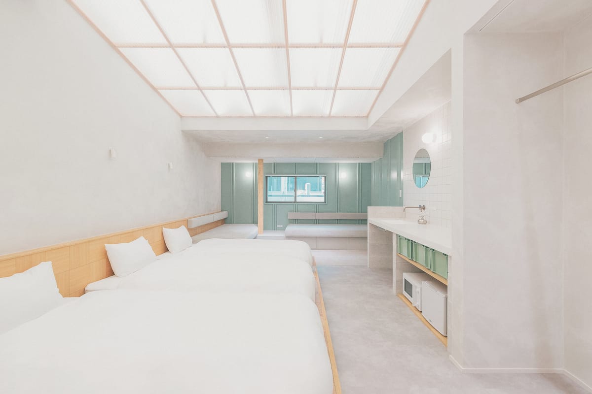 A modern hotel room with a large bed, a vanity with a mirror, and a bench.