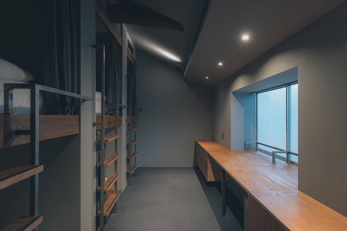 A narrow, dimly lit room with a wooden desk and shelves, a window with a view, and a ceiling with recessed lighting.