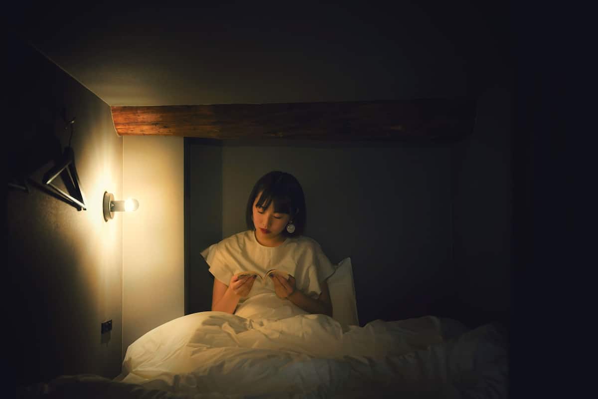 A dimly lit room with a person sitting on a bed, reading a book.