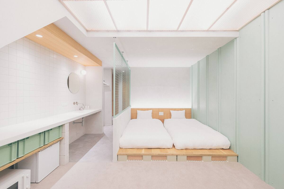 A modern hotel room with a bed, a vanity with a mirror, and a green storage unit.
