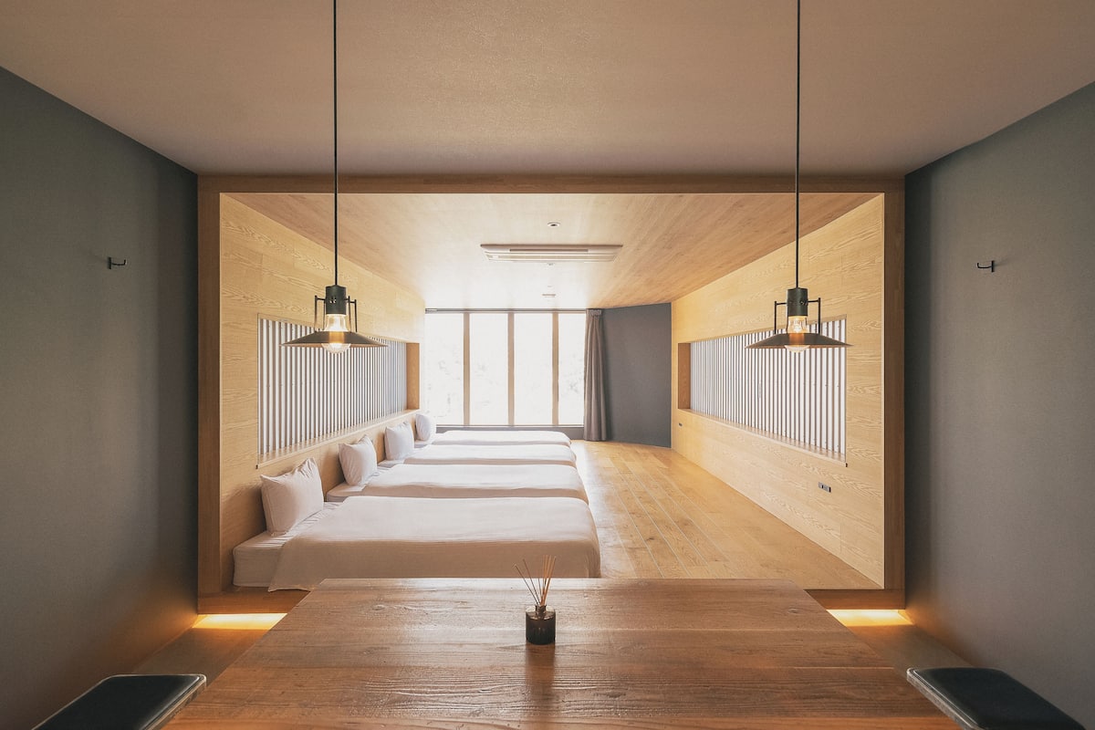 A modern hotel room with a wooden floor, a central table with a vase, and a bed with a headboard.