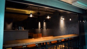A modern bar area with wooden tables and orange seating, under industrial-style pendant lighting. - SEKAI HOTEL Deep Osaka Experience - Hostel (Higashi-osaka)