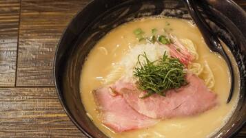 A bowl of ramen with noodles, pork, and toppings on a wooden table.