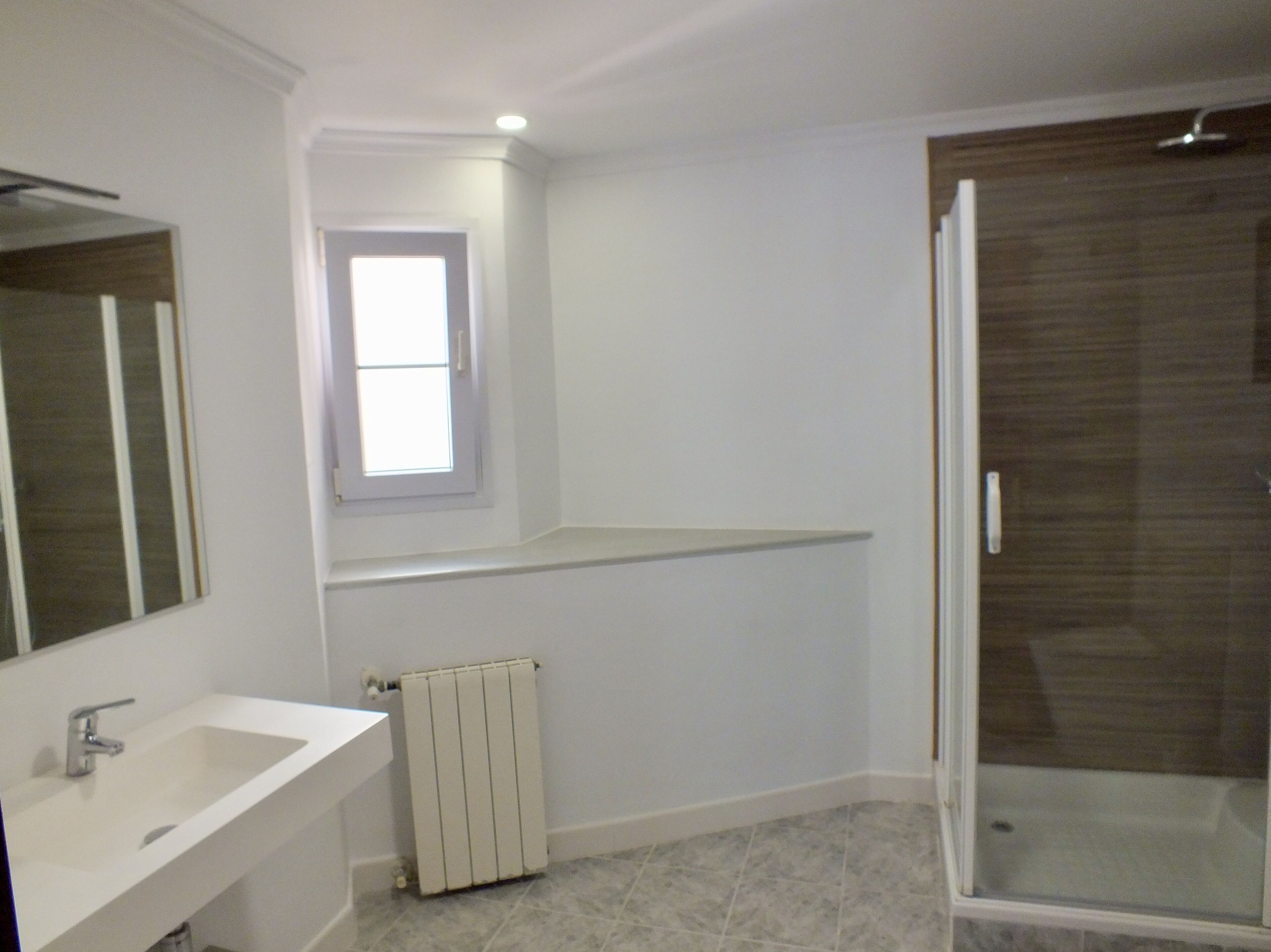 Une salle de bain moderne avec un lavabo blanc, un miroir, une fenêtre, un radiateur et un espace douche.