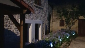 A stone building with a wooden porch and a garden with flowers and a tree. - A beautifully restored stone property overlooking the stunning Charente river.  (Luxé)