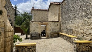 A courtyard with stone walls, a wooden bench, and a metal table. - A beautifully restored stone property overlooking the stunning Charente river.  (Luxé)