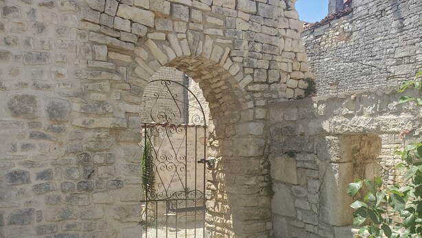 An arched stone doorway with a metal gate, surrounded by stone walls and vegetation. - A beautifully restored stone property overlooking the stunning Charente river.  (Luxé)
