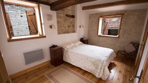 A bedroom with a wooden floor, a bed with floral bedding, a nightstand, a dresser, and a window with a view of a stone wall. - A beautifully restored stone property overlooking the stunning Charente river.  (Luxé)