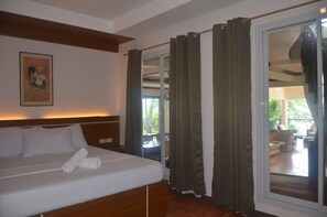 A hotel room with a bed, a painting on the wall, and a view of the outdoor patio area through a sliding glass door.