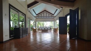 A spacious room with a tiled floor, a central seating area with chairs, and a large window allowing natural light. - Robinland Vacation Home Badian (Alegria)
