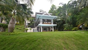 A modern two-story house with a covered porch, surrounded by lush greenery and palm trees. - Robinland Vacation Home Badian (Alegria)