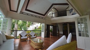 A spacious indoor area with wicker furniture, a glass table, and a balcony with a railing. - Robinland Vacation Home Badian (Alegria)