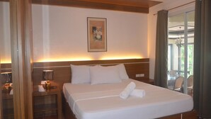 A hotel room with a large bed, a bedside table with a lamp, a painting on the wall, and a view of the outdoors through a window. - Robinland Vacation Home Badian (Alegria)