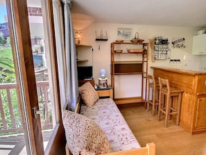 A cozy room with a sofa, a small table, a TV, and a kitchen area with a bar.