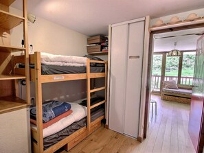 A bunk bed room with a wooden floor, a white door, and a view of a balcony with outdoor furniture.
