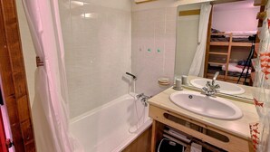 Een badkamer met een bad, twee wastafels, een spiegel en een douche.