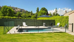 Ein Swimmingpool mit umzäuntem Deck, Liegestühlen und Blick auf eine Hügelstadt.